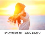 Enjoyment - free happy woman enjoying sunset. Beautiful woman in white dress embracing the golden sunshine glow of sunset with arms outspread and face raised in sky enjoying peace, serenity in nature