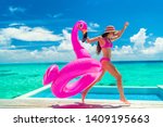 Vacation fun woman in bikini with funny inflatable pink flamingo pool float running of joy jumping by infinity swimming pool. Girl enjoying travel holidays at resort luxury overwater bungalow travel.