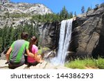 Hikers resting in Yosemite National park enjoying view of beautiful waterfall, Vernal Fall. Young hiking couple relaxing after hike in beautiful summer nature landscape.