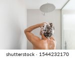 Man taking a shower washing hair under water falling from rain showerhead in luxury walk-in bath. Showering young person at home lifestyle. Body care morning routine in sunlight.
