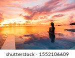 Paradise sunset idyllic vacation woman silhouette swimming in infinity pool looking at sky reflections over ocean dream. Perfect amazing travel destination in Bora Bora, Tahiti, French Polynesia.