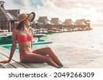 Suntan bikini body Asian woman relaxing sunbathing at luxury vacation in paradise Bora Bora high end resort hotel by the swimming pool at overwater villa suite.