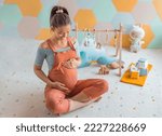 Pregnant woman smiling at belly in nursery playrooom with Baby activity gym play, toys and playmat. Pregnancy concept and home nusery planning and decoration concept photo with happy expecting woman