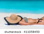 Beach relaxation woman sleeping sun tanning covering her face with straw hat for uv solar protection on caribbean destination blue ocean background. Vacation girl relaxing resting on summer travel. 