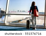 Travel tourist standing with luggage watching sunset at airport window. Unrecognizable woman looking at lounge looking at airplanes while waiting at boarding gate before departure. Travel lifestyle.