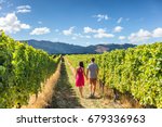 Vineyard couple tourists New Zealand travel visiting winery walking amongst grapevines. People on holiday wine tasting experience in summer valley landscape.