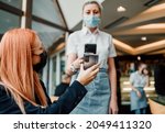 Young attractive business woman sitting in a restaurant or cafe bar and showing digital Covid-19 immunization pass certificate to the waitress. Pandemic and global security measures concept.