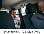 Good looking young business woman sitting on backseat in luxury car. She using her smart phone and smiling. Transportation in corporate business concept.