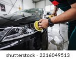 Small photo of Professional car service worker polishing luxury car with orbital polisher in a car detailing and valeting shop. Ultra wide angle shot.