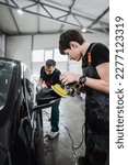 Small photo of Professional car service worker polishing luxury car with orbital polisher in a car detailing and valeting shop. Ultra wide angle shot.