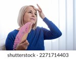 Small photo of Mature woman experiencing hot flush from menopause at home. With sweat glistening on her forehead, a middle-aged woman clutches a fan to her chest in an attempt to alleviate the symptoms of menopause