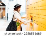 Small photo of Fashion woman with box using modern postal automatic mail terminal with self service device for pickup or refund an order. Electronic locker for storing parcels. Online shopping. Selective focus