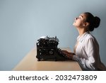 happy young woman is an author at a typewriter, is inspired, is passionate about writing a text. A writer at a table with a vintage typewriter, on a blue background