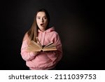 Small photo of A stunning plot twist in a bestseller, a young brunette reads a book in shock. A student in pink with an open book in her hands