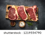 Raw meat beef steak. Black angus prime meat set - ribeye, striploin, t-bone steaks on cutting board. Top view on black table.