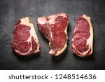 Dry aged beef steaks - ribeye, striploin, t-bone steaks on Black slate background. Top view with copy space.