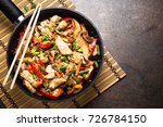 Chicken stir fry with   vegetables soy sause and sesame in the wok. Traditional asian food. Top view wiht copy space on stone table.