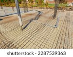 Small photo of Pump hose is pouring fresh concrete over square reinforcement in the base of new building covering sanitary pipeline, set of embed plastic pipes for sewer.