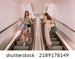 Small photo of Two young girls passing by eachother on the escalator in the shopping mall