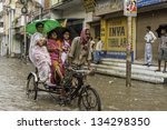 Small photo of VARANASI, INDIA - AUGUST 11: Cycle rickshaw and passengers try to make headway through flood waters after monsoon storm in a busy street on August 11, 2011 in Varanasi, Uttar Pradesh, India.