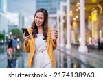 Urban modern lifestyle fashion portrait of asian young female stylish casual Asia woman walking 
with coffee cup and smartphone connection on the street, wearing cute trendy outfit after raining