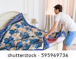 Small photo of handsome young man making bed a color patchwork quilt in the white interior. scrappy blanket on the bed closeup.